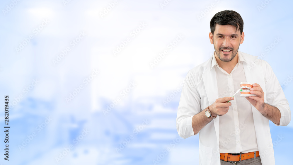 Young male dentist showing toothbrush and denture in dental clinic. Selective focus at the toothbrus