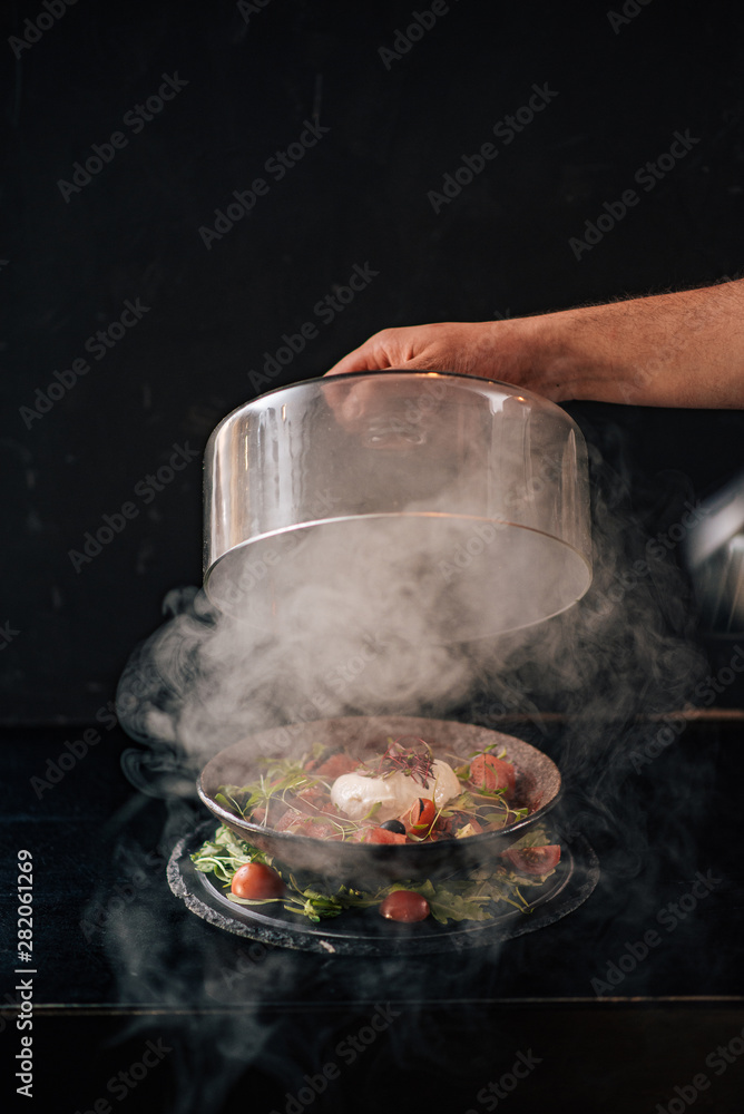 美食。在深色背景下，用手在烧焦的caprese沙拉上涂上肉酱。