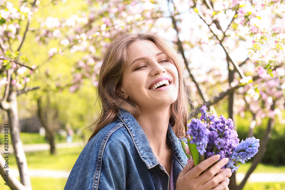 Beautiful young woman with bouquet of flowers in park on spring day