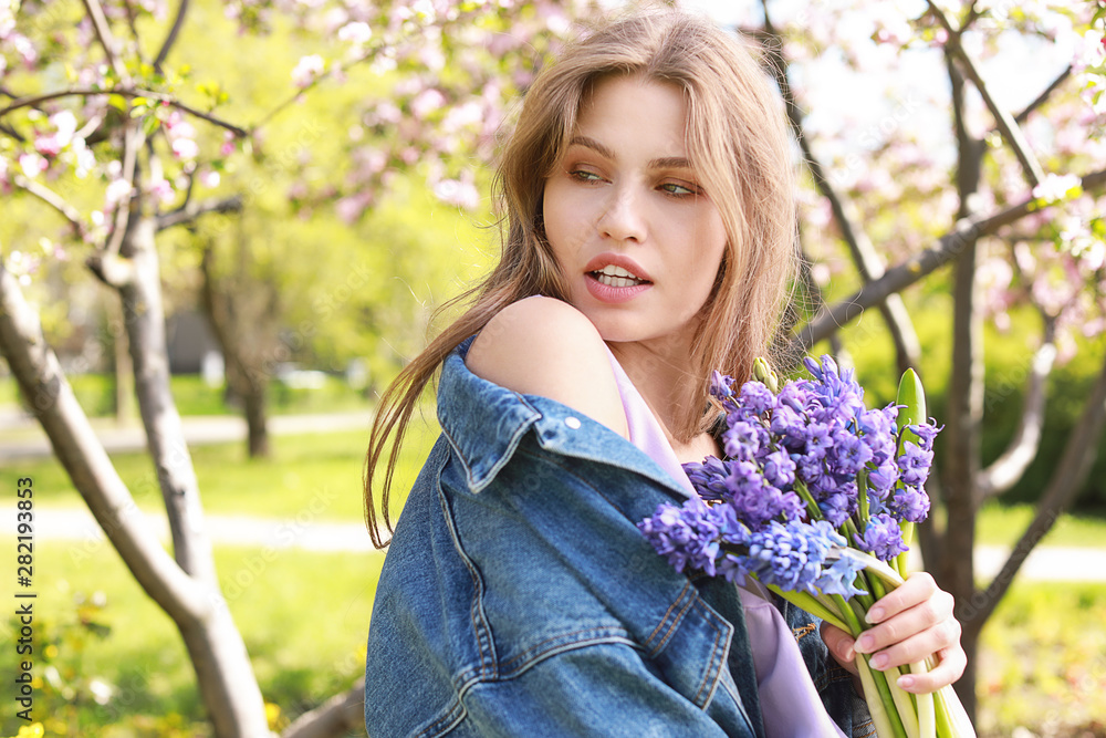 Beautiful young woman with bouquet of flowers in park on spring day