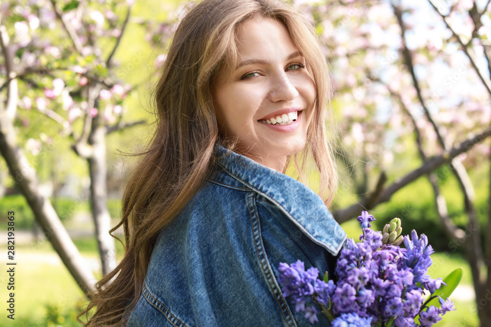 Beautiful young woman with bouquet of flowers in park on spring day