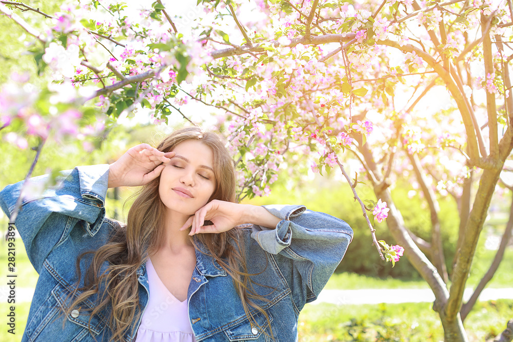 Beautiful young woman near blooming tree on spring day