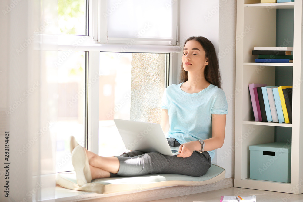 Female student with laptop preparing for exam near window