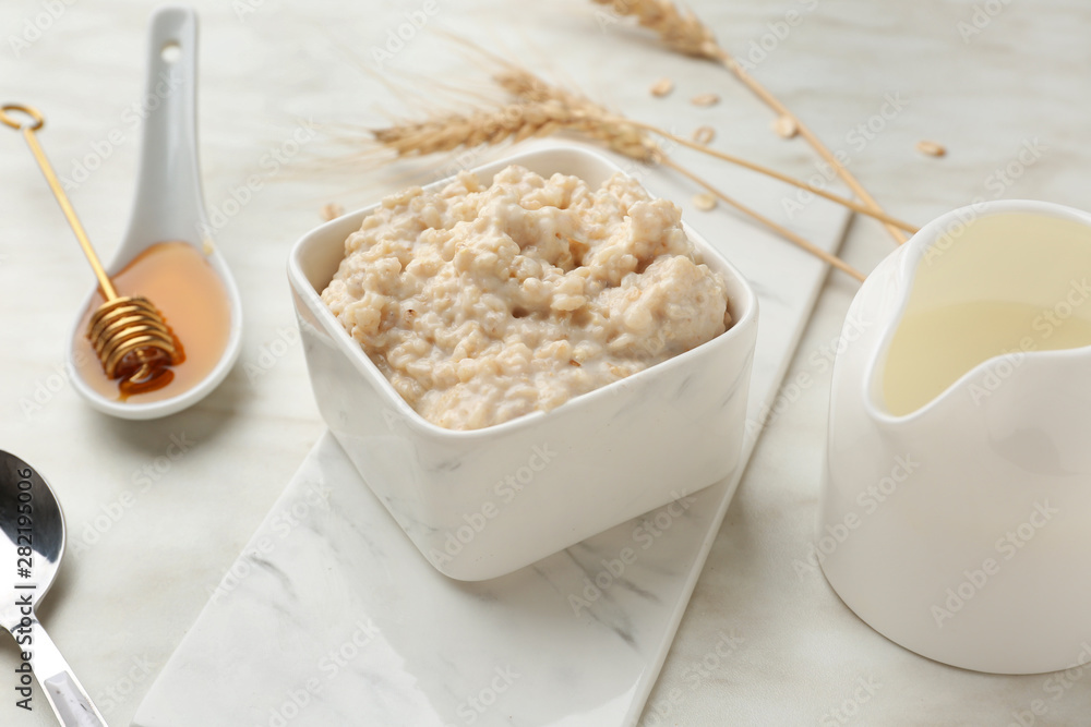 Bowl with tasty oatmeal, milk and honey on light table