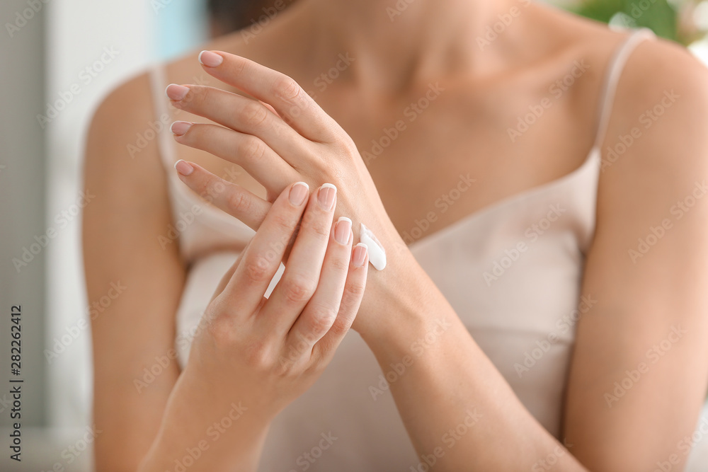 Young woman applying natural cream onto skin at home