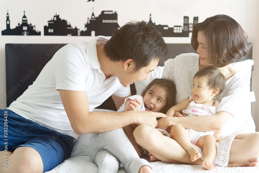 Happy family concept. Asian father teasing and playing to their kids sitting on the bed. The childre