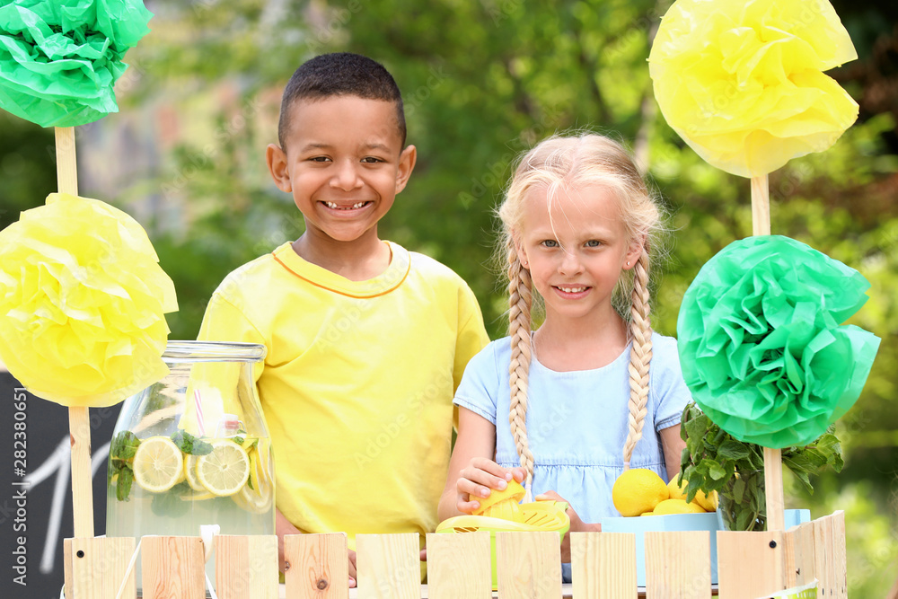 Cute little children selling lemonade in park