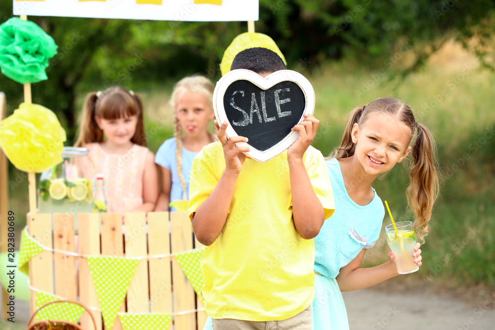 Cute little children selling lemonade in park