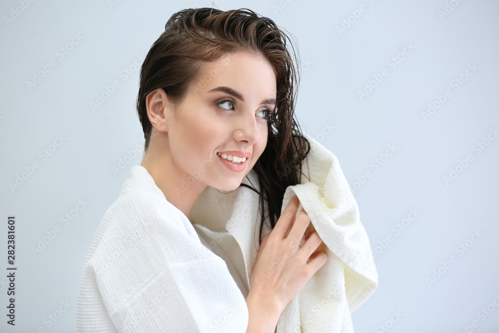 Beautiful young woman wiping hair after washing against light background