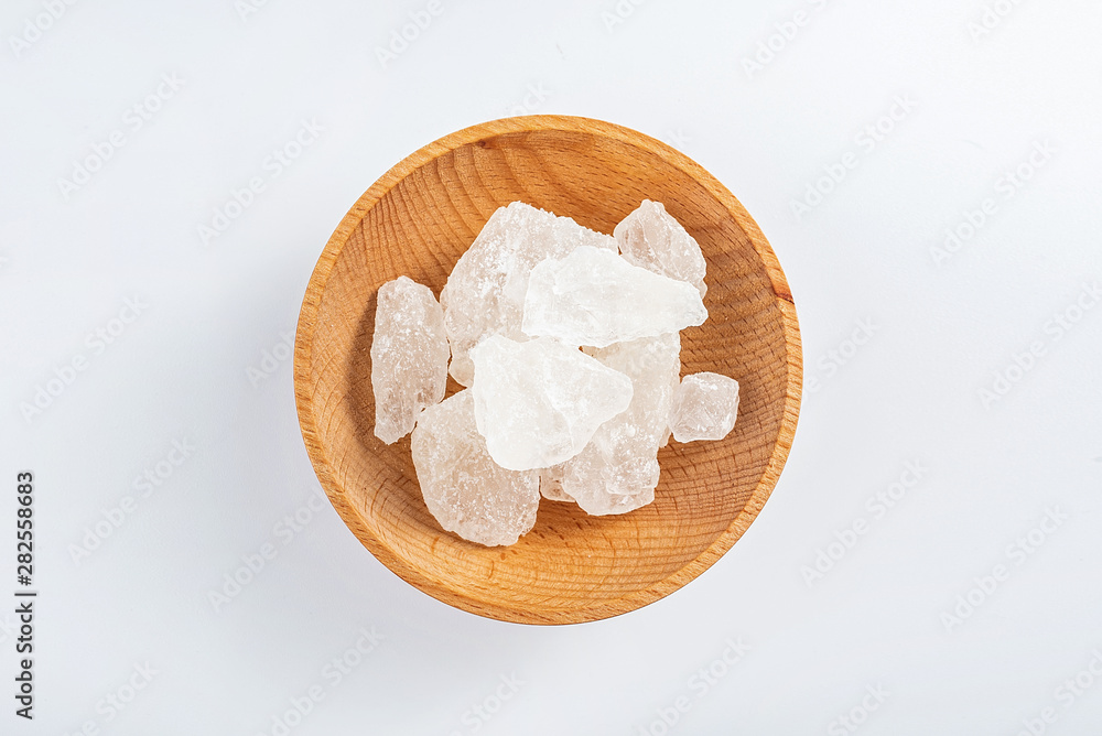 Polycrystalline crystal sugar filled with a wooden dish on a white background