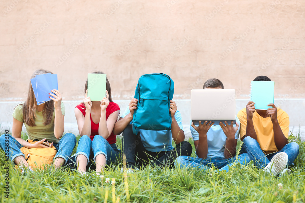 Young students hiding faces while sitting on grass outdoors