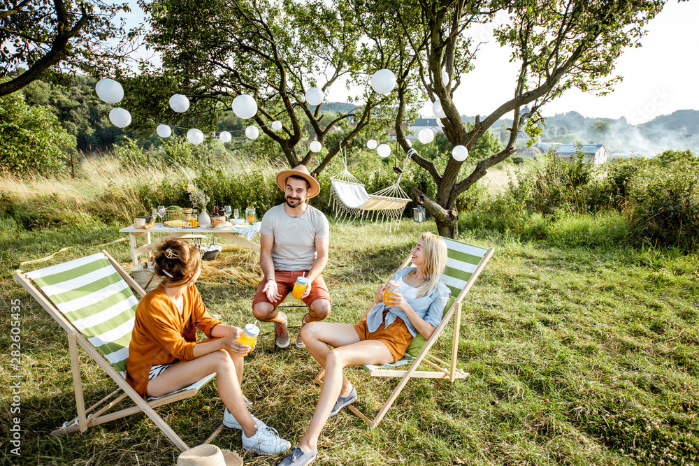 Young and cheerful friends relaxing with drinks, sitting on the sunbeds in the beautifully decorated