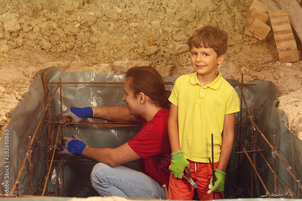 Little boy helps father to knit metal framework