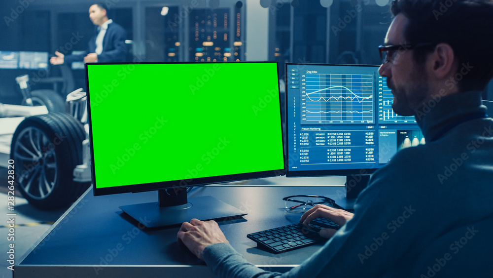 专业工程师在带有绿屏模型的计算机上工作并测试电动汽车底盘