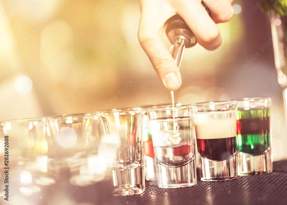 Cropped photo of barman pouring liquor from shaker to set of shot cocktails