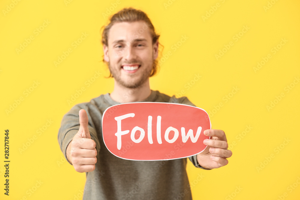 Male blogger holding paper with text FOLLOW on color background