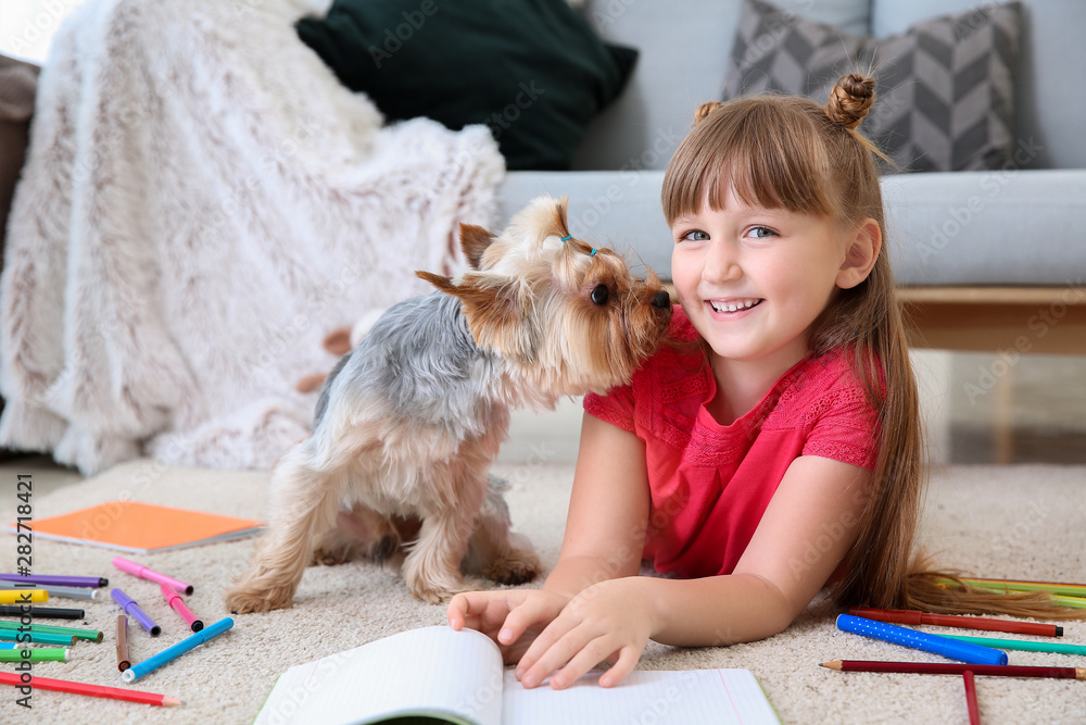 Little girl with cute dog drawing while lying on carpet