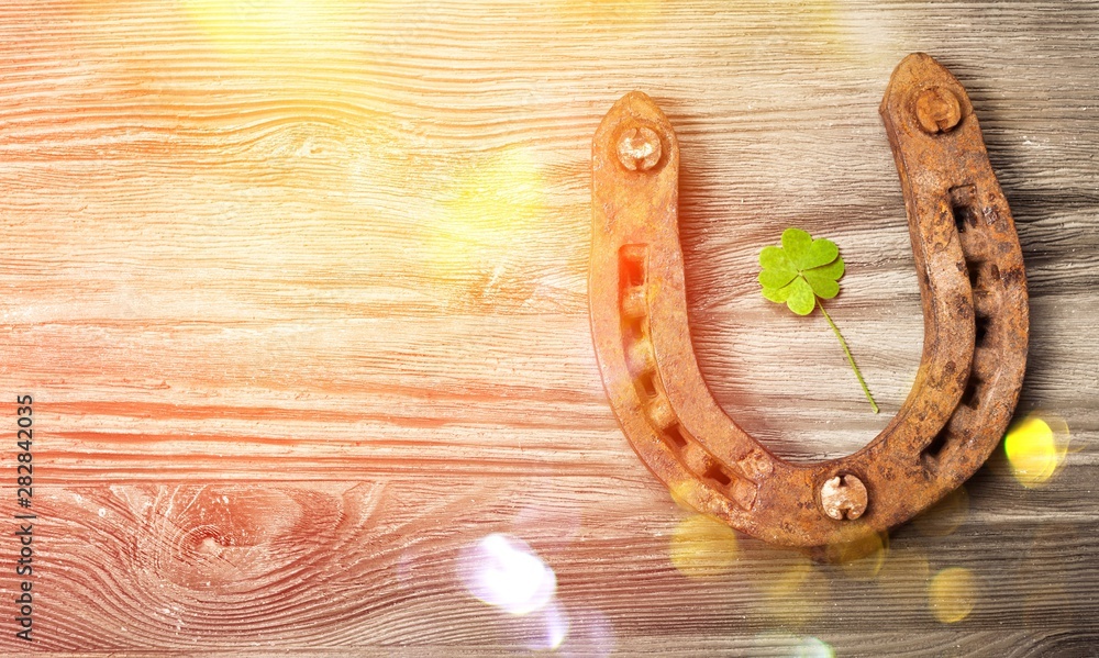 Rusty metal horseshoe with a leaf of clover on a wooden table