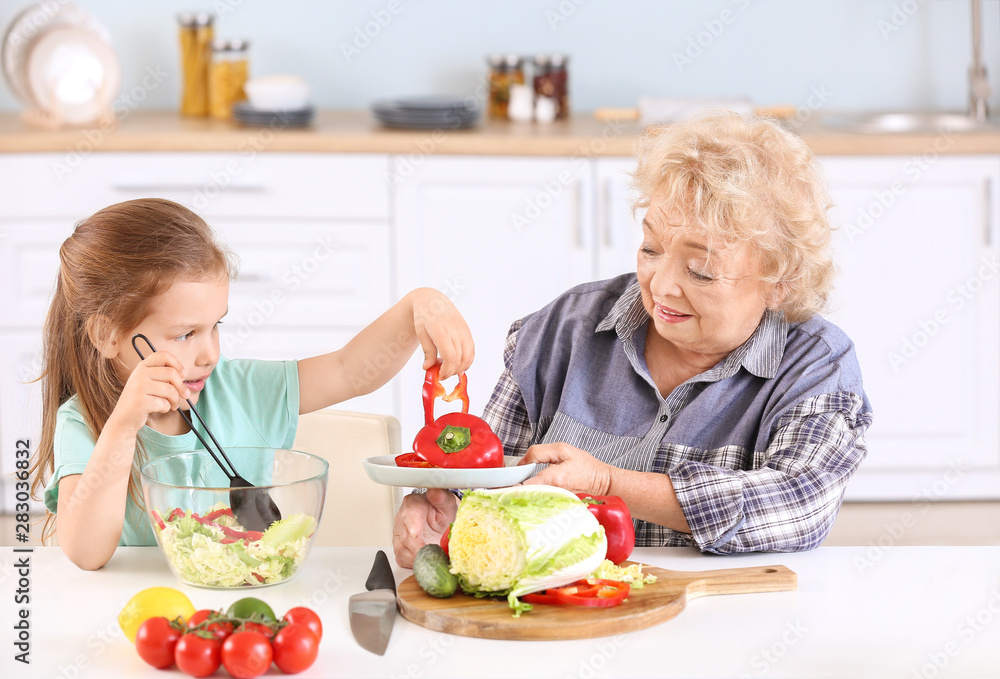 Cute little girl with grandmother preparing vegetable salad in kitchen