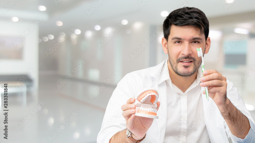 Young male dentist showing toothbrush and denture in dental clinic. Selective focus at the toothbrus