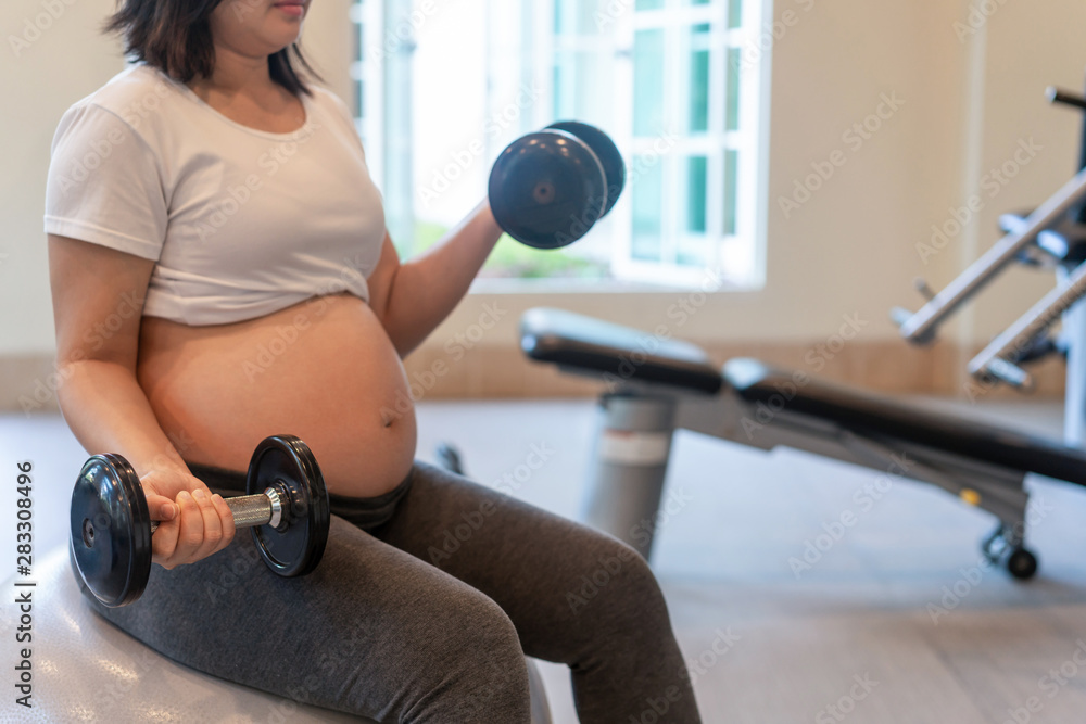 Active pregnant woman exercise in fitness center at yoga room. The young expecting mother holding ba