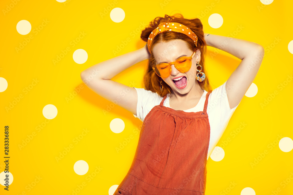 Fashion model girl over yellow polka dots background. Beauty stylish redhead woman posing in urban c