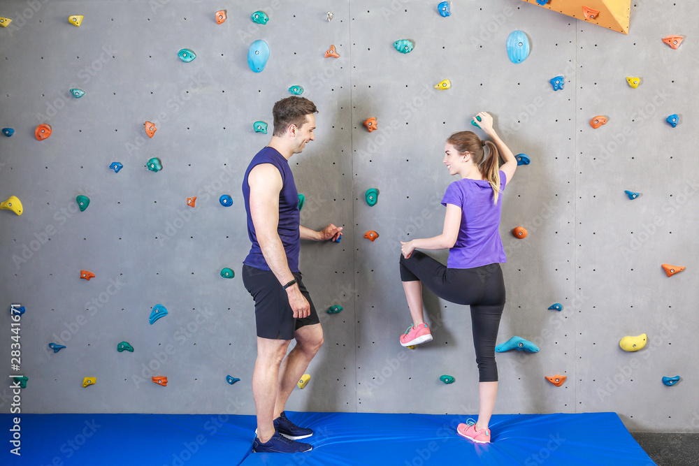 Instructor teaching young woman to climb wall in gym