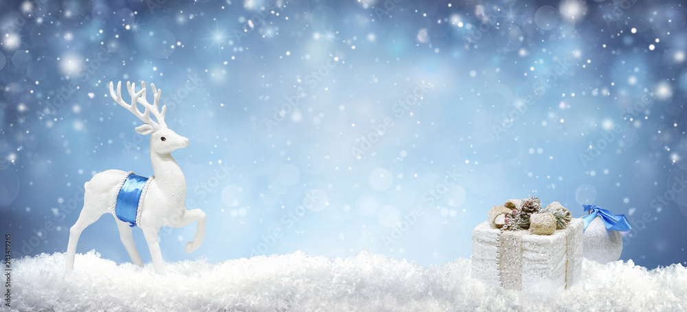 Christmas background with white decorative deer and gift box in snow on evening blue sky background 