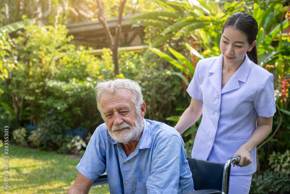 Depressed thoughtful elderly man on wheelchair with nurse in garden at nursing home