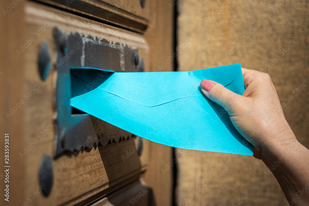 Woman inserting blue envelope into mail slot. Delivering letter by mail carrier