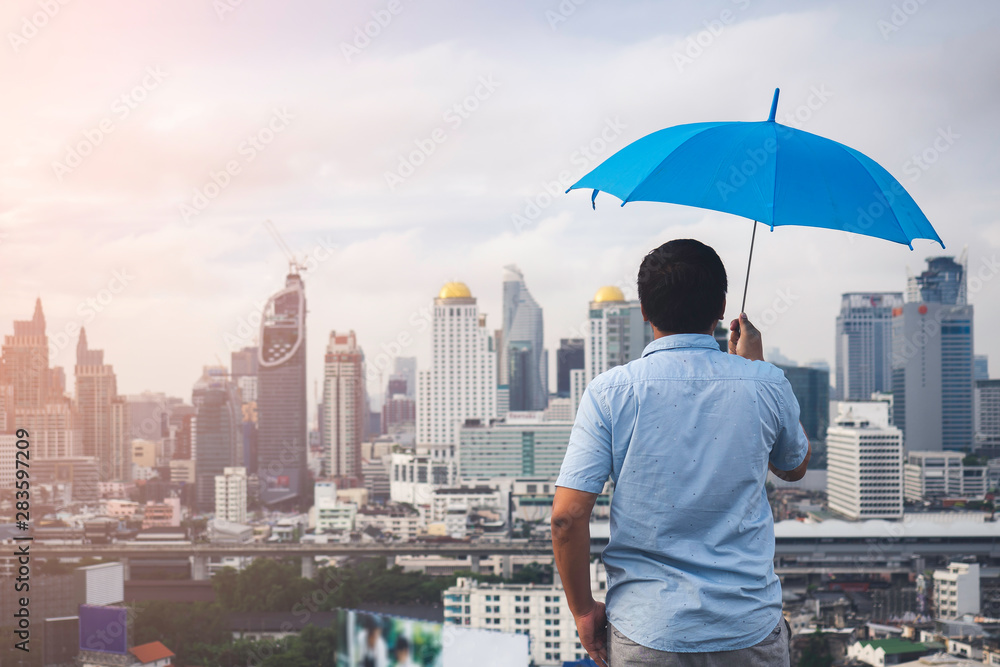 手持蓝色雨伞遮雨的男子的后视图