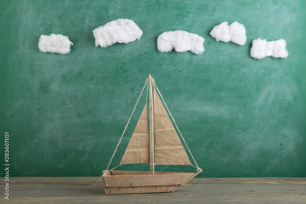 Education is a journey concept, toy boat under cotton clouds on the chalkboard background, inspirati