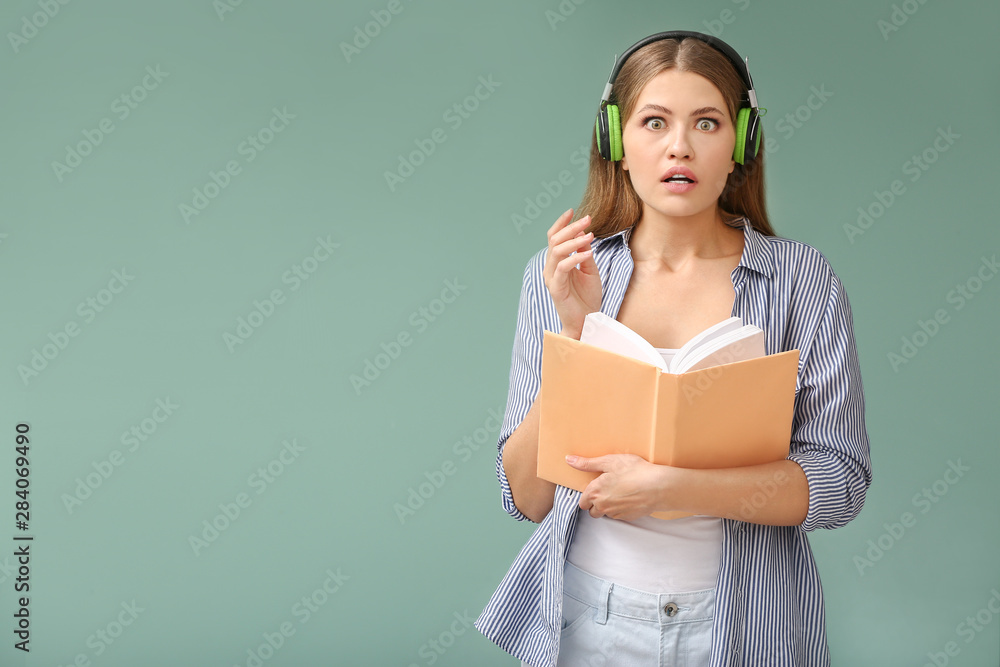 Shocked young woman listening to audiobook on color background