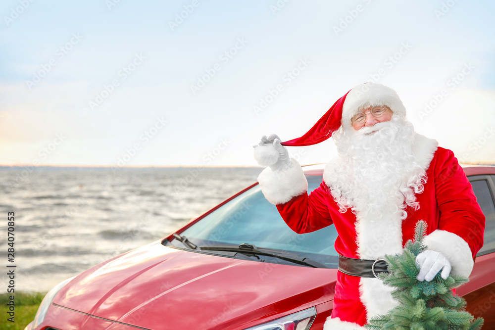 Santa Claus with fir tree near car on riverside