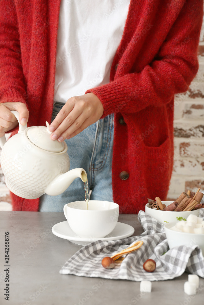 Woman pouring tasty hot beverage from teapot into cup at table