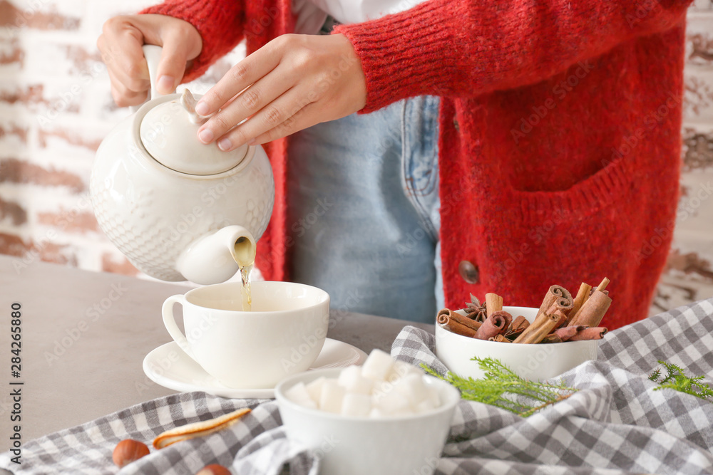 Woman pouring tasty hot beverage from teapot into cup at table