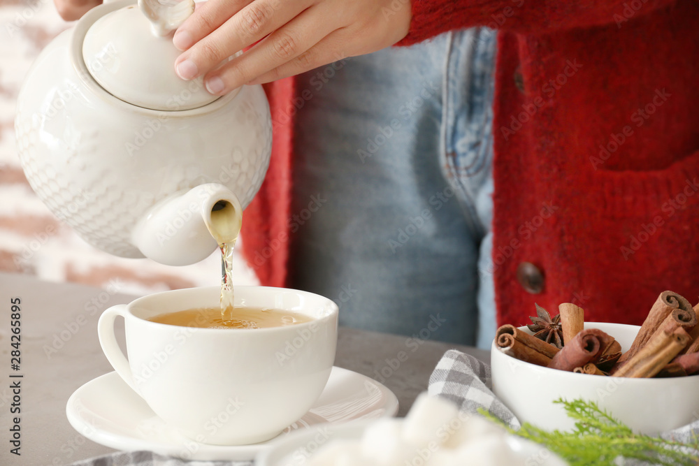 女人把美味的热饮从茶壶里倒进桌子上的杯子里