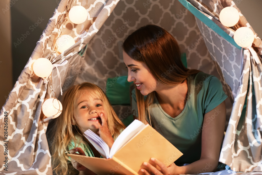 Happy woman with her little daughter reading book in hovel at home