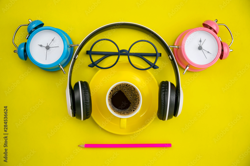 Top view of coffee cup with headphone,alarm clock,pencil and teacher glasses on yellow paper backgro