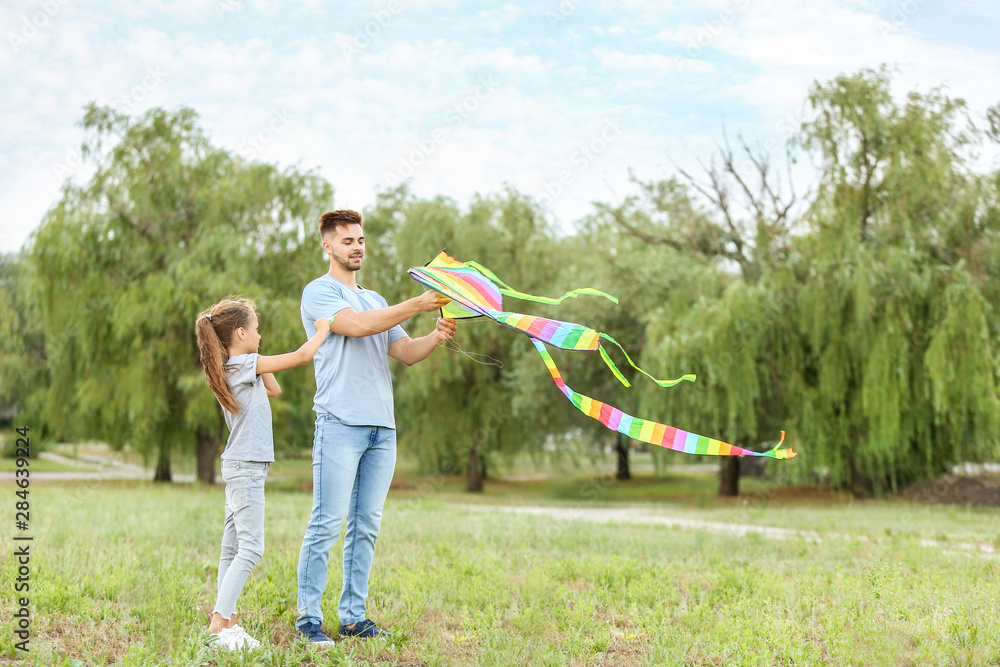 Young man with little daughter flying kite outdoors