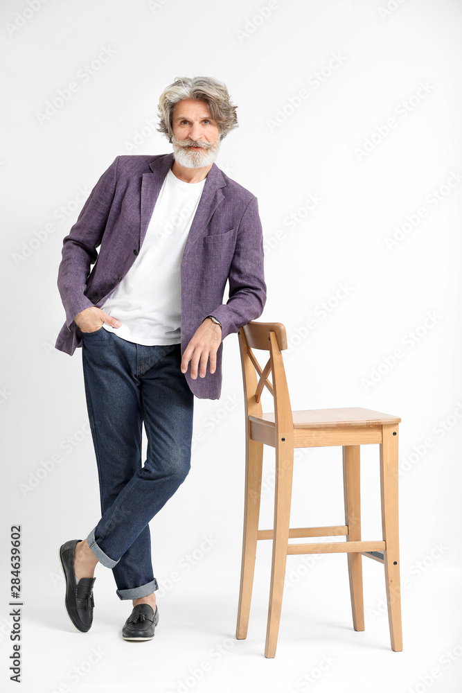 Fashionable senior man with chair on light background