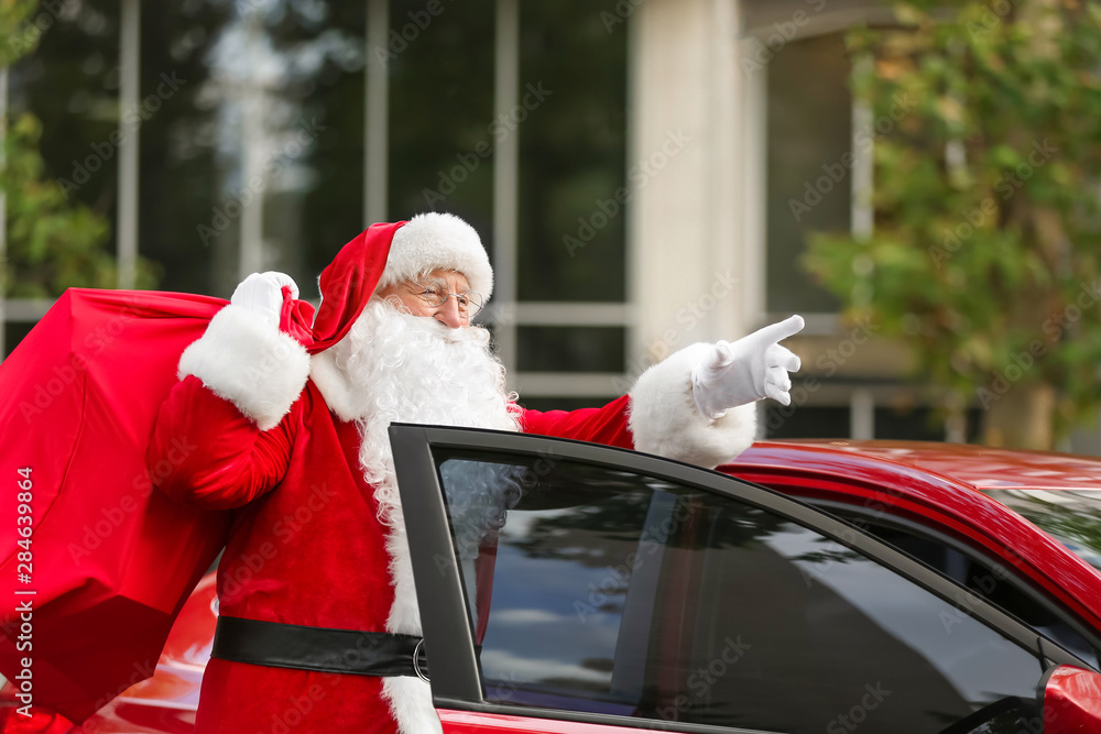 Santa Claus with gifts in bag near car outdoors