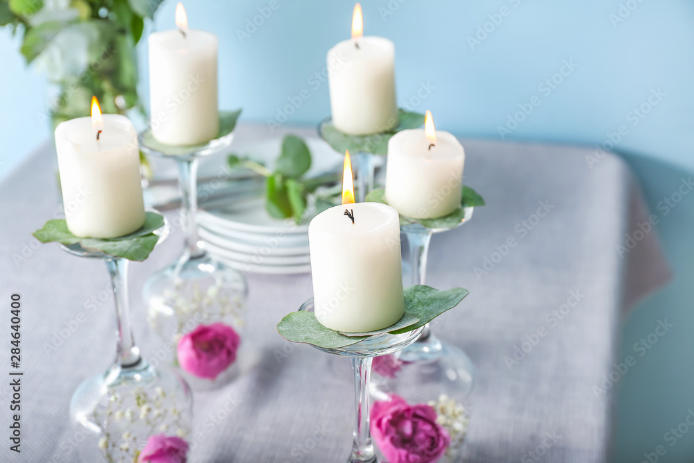 Glasses with flowers and burning candles on table