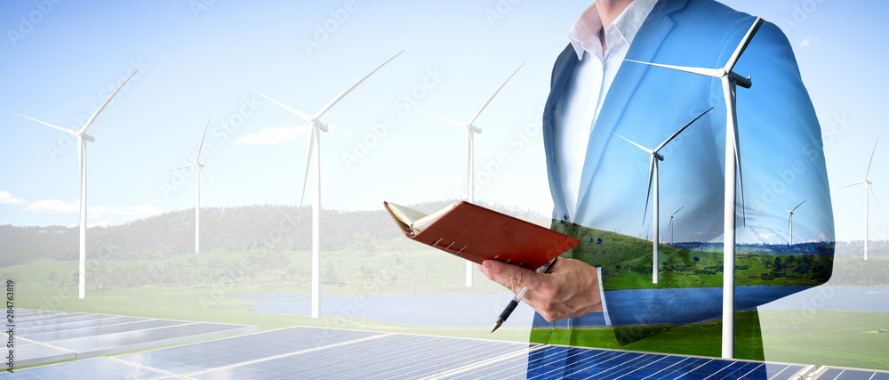 Double exposure graphic of business people working over wind turbine farm and green renewable energy