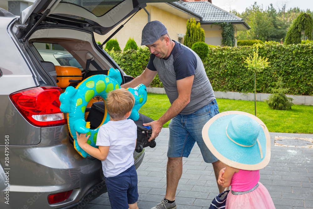 Father with little son and daughter are loading the car trunk with luggages for holidays