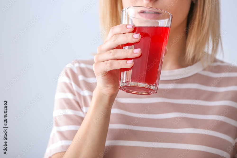 Woman drinking tasty pomegranate juice on light background, closeup