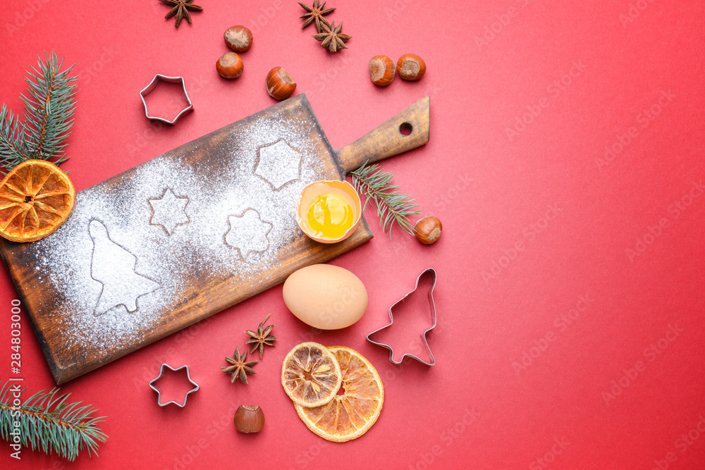 Wooden board with cookie cutters and ingredients on color background