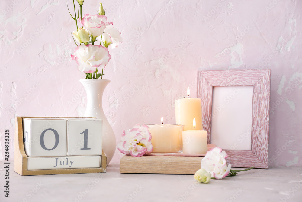 Beautiful candles, calendar, flowers and blank photo frame on table