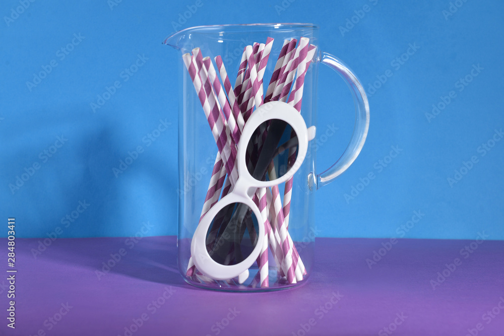 Jug with straws and sunglasses on color table