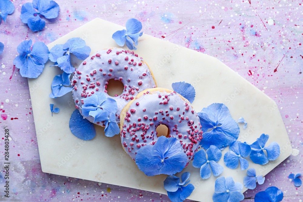 Sweet tasty donuts and flowers on color background